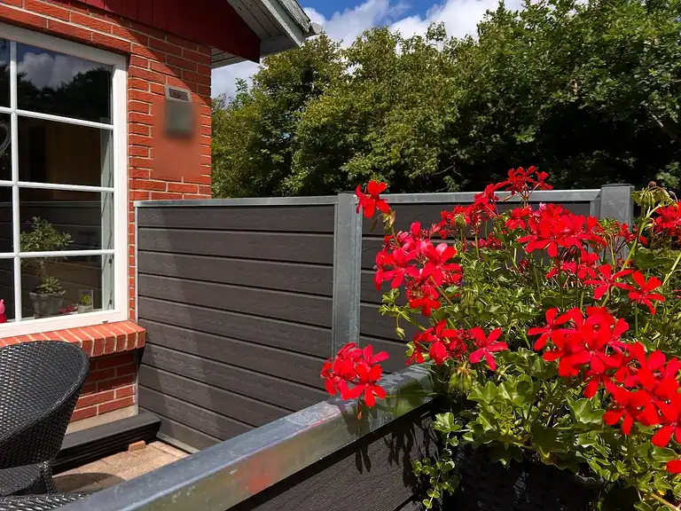 Komposithegn med blomsterkasse og røde pelargonier ved husets hjørne