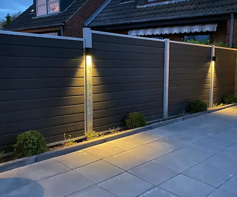 Komposithegn med lys i stålstolperne ved en terrasse i skumringen