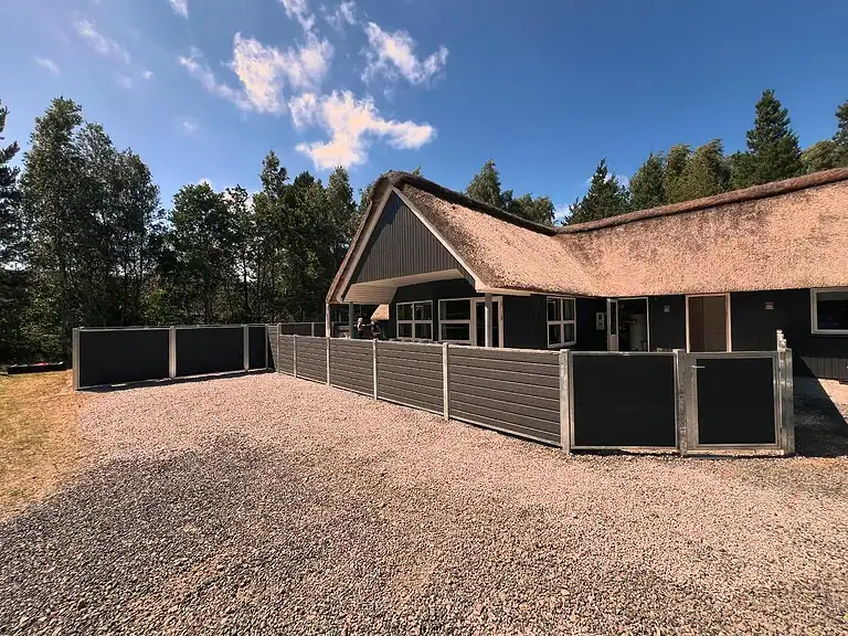 Komposithegn med galvaniserede stolper ved et sommerhus med stråtag
