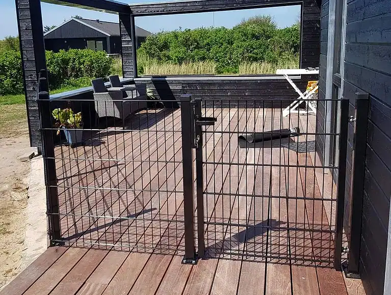 Sort 2D-panelhegn med rammeløs låge ved en terrasse
