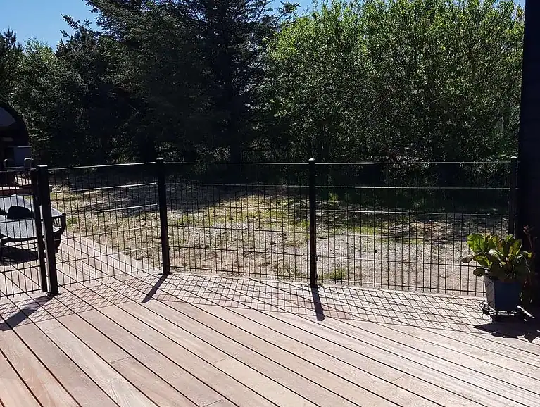 Sort 2D-panelhegn langs terrassen med naturgrund bagved