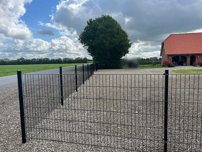 Sort panelhegn omkring en gårdsplads
