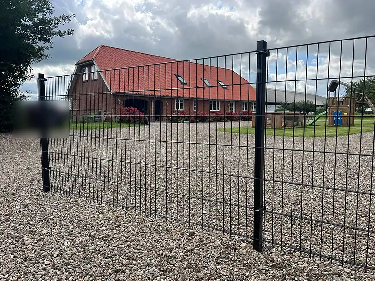 Sort panelhegn ved et murstenshus med rødt tag