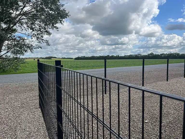 Sort panelhegn langs en grusplads