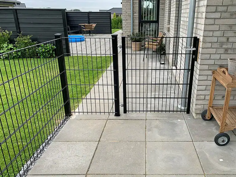 Rammeløs låge i sort 2D-panelhegn ved en terrasse